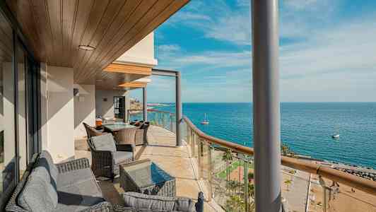 En balkon med siddepladser og udsigt over havet og stranden. (AI-genereret tekst)