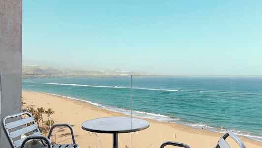 Udsigt fra en balkon mod en sandstrand og havet. (AI-genereret tekst)