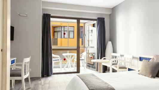 Hotelværelse med to senge, siddeområde og en balkon i baggrunden. (AI-genereret tekst)