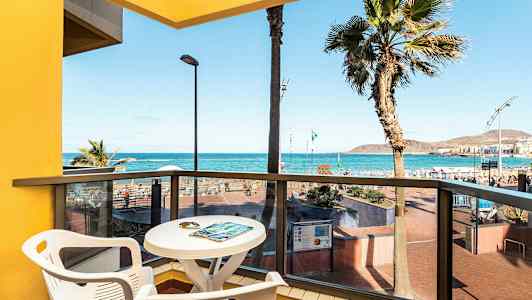 Udsigt fra en altan med bord og stole mod havet og stranden. (AI-genereret tekst)