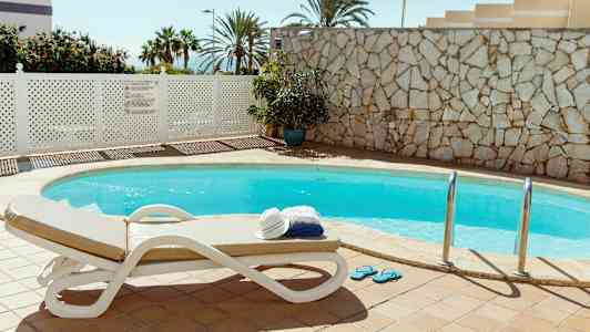 Udendørspool med liggestol og en stak håndklæder og hat. (AI-genereret tekst)