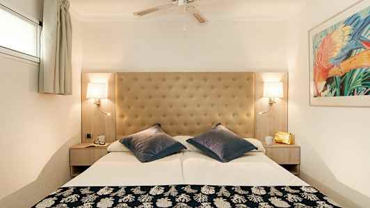 Et hotelværelse med en dobbeltseng, polstret sengegavl, loftsventilator og væglamper. (AI-genereret tekst)