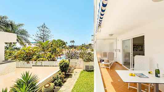 En terrasse med stol og bord, udsigt til en have med palmer. (AI-genereret tekst)