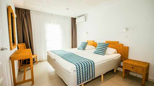 Et hotelværelse med to enkeltsenge, bambusmøbler og hvide vægge. (AI-genereret tekst)