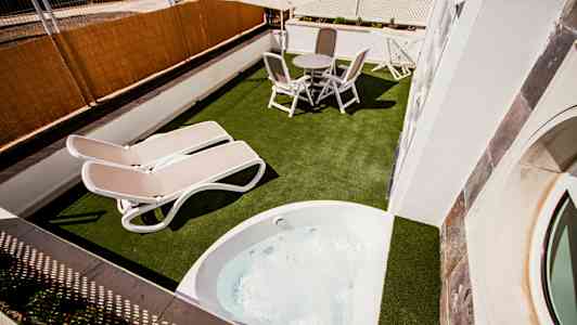 En terrasse med bord, stole, to solsenge og et boblebad. (AI-genereret tekst)