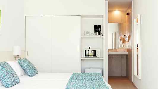 Et hotelværelse med en seng, lamper og et tekøkken, der inkluderer en mikrobølgeovn og en kaffemaskine. (AI-genereret tekst)