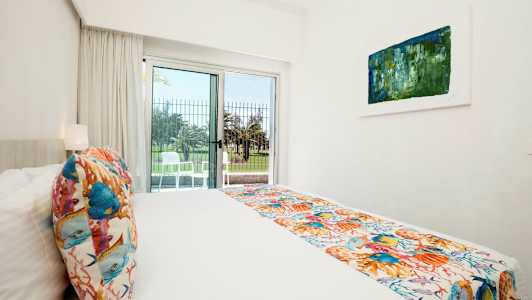 Et lyst hotelværelse med en seng, farverige dekorationer og en åbning til en terrasse. (AI-genereret tekst)