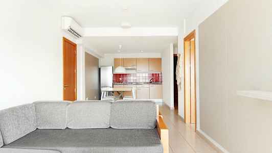 Billede af en lys stue med en grå sofa i forgrunden og et køkken i baggrunden. (AI-genereret tekst)