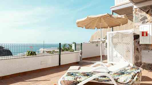 Solstol med parasol på en terrasse med havudsigt. (AI-genereret tekst)