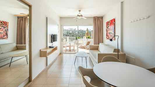 Et moderne hotelværelse med to sofaer, spisebord og stole samt en altan med udsigt. (AI-genereret tekst)