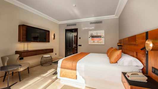 Et hotelværelse med en stor seng, orange sengetøj og en moderne indretning. Et TV er monteret på væggen. (AI-genereret tekst)