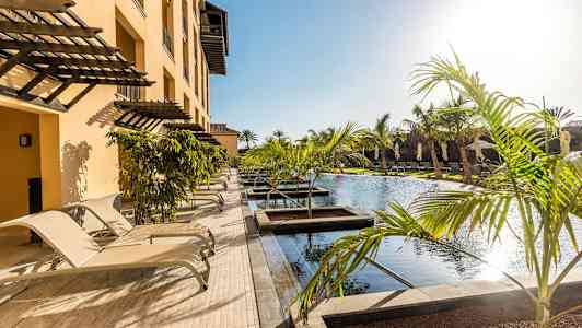 En pool med omkringliggende liggestole og palmer ved et hotel. (AI-genereret tekst)