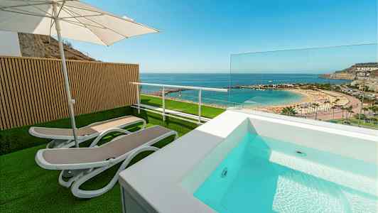 Terrasse med liggestole, parasol og lille pool med udsigt over strand og hav. (AI-genereret tekst)