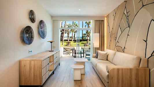 Et moderne indrettet opholdsstue med trædetaljer og en beige sofa, udsigt til en grøn have gennem glasdøre. (AI-genereret tekst)