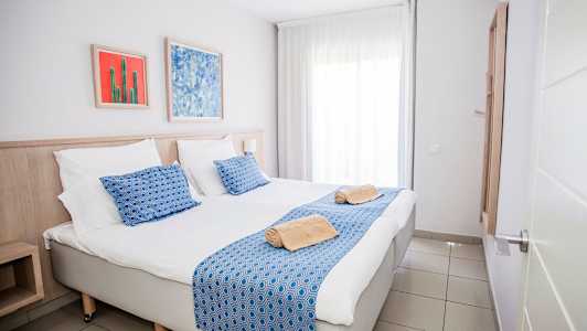 Billede af et hotelværelse med en dobbeltseng, blå detaljer og kunstværker på væggen. (AI-genereret tekst)