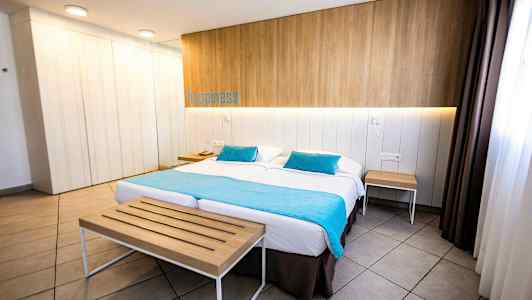 Et hotelværelse med en dobbeltseng, træpanel på væggen, turkise tekstiler og borde ved siden. (AI-genereret tekst)