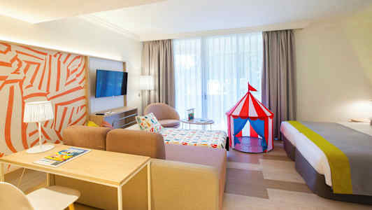 Et hotelværelse med et farverigt cirkustelt-legetøj ved siden af sengen. (AI-genereret tekst)