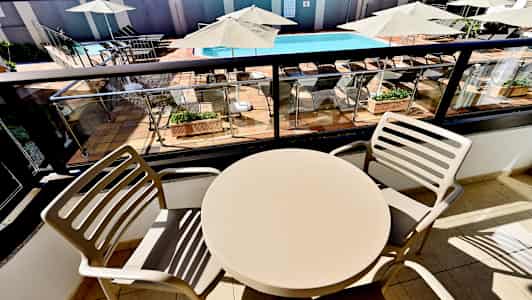 Et bord med to stole på en altan med udsigt over en pool og liggestole. (AI-genereret tekst)