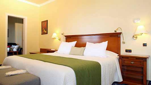 Et hotelværelse med en bred seng, grønt sengedække og trægulv. (AI-genereret tekst)