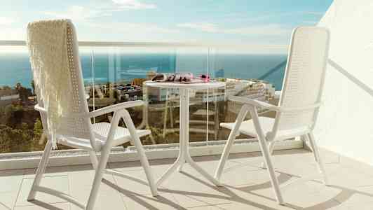To hvide stole og et bord på en altan med udsigt over havet. (AI-genereret tekst)