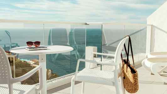 En terrasse med hvide møbler, en stråtaske og havudsigt. (AI-genereret tekst)