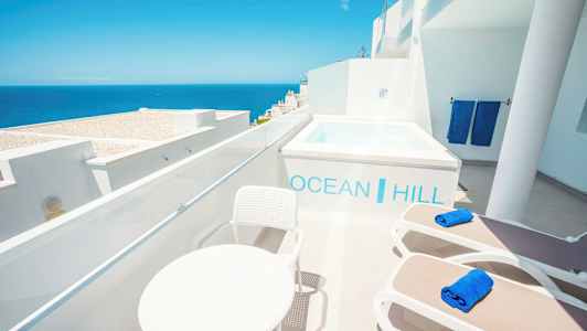 Terrasse med udsigt over havet, liggestole, bord og en lille pool. (AI-genereret tekst)