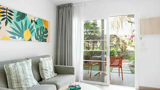 Stuemiljø med grå sofa, puder, farverigt vægkunst og glasdør, der fører til terrasse. (AI-genereret tekst)