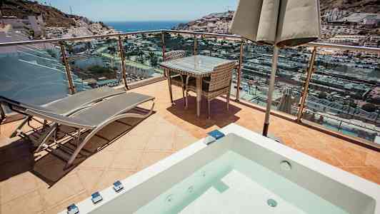 Terrasse med liggestole, bord og udsigt over havet og byen. (AI-genereret tekst)