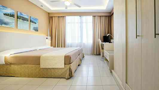 Et hotelværelse med en dobbeltseng, et skrivebord og en loftsventilator. (AI-genereret tekst)