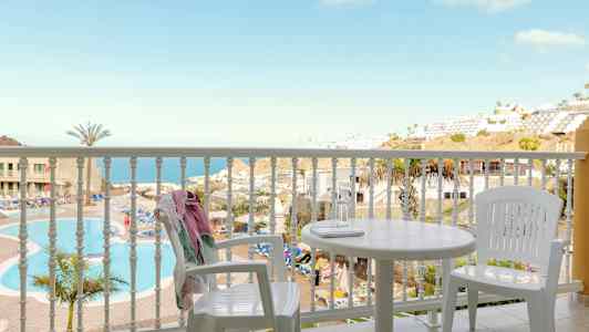 Udsigt fra en altan med hvide møbler mod en pool og en havudsigt. (AI-genereret tekst)