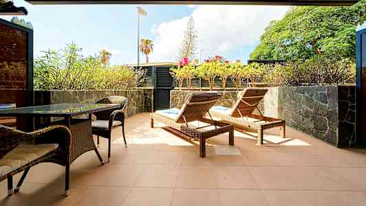 En terrasse med liggestole, bord og stole samt omgivet af planter. (AI-genereret tekst)