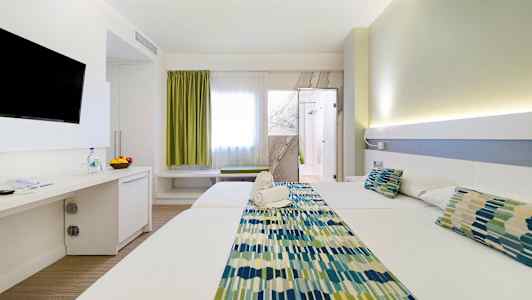 Et hotelværelse med to senge, et tv på væggen og en dør til badeværelset. Værelset har lys indretning. (AI-genereret tekst)