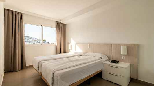 Et hotelværelse med en dobbeltseng og et vindue, der viser en hvid bygning. (AI-genereret tekst)