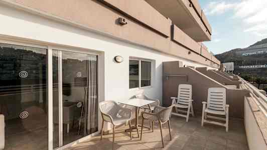 En terrasse med bord, stole og solsenge, samt udsigt til de omkringliggende bygninger og bjerge. (AI-genereret tekst)