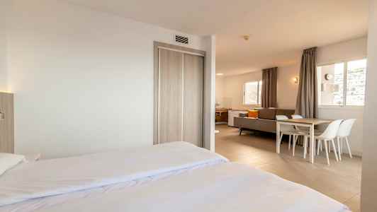 Moderne og lyst indrettet hotelværelse med dobbeltseng, siddegruppe og spisebord. (AI-genereret tekst)