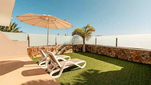 En udendørs terrasse med to liggestole, parasol og kunstgræs. (AI-genereret tekst)