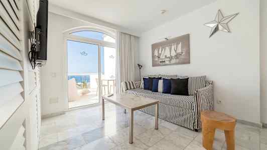 Sort-hvidt interiør med sofa og bord i et rum med udsigt gennem glasdøre til havet. (AI-genereret tekst)