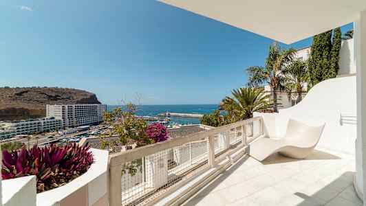 Udsigt fra en solterrasse over havet og en havn. (AI-genereret tekst)