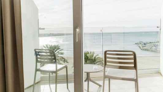 Udsigt fra en altan med to stole og et bord, mod en strand og havet. (AI-genereret tekst)