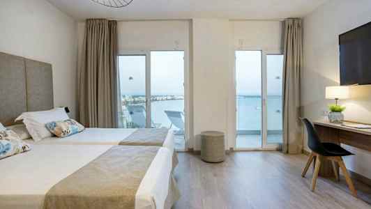 Hotelværelse med to enkeltsenge, skrivebord og havudsigt gennem glasdøre. (AI-genereret tekst)