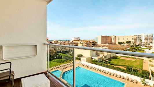 Altan med udsigt over en swimmingpool og omkringliggende bygninger. Liggestole står ved poolen. (AI-genereret tekst)