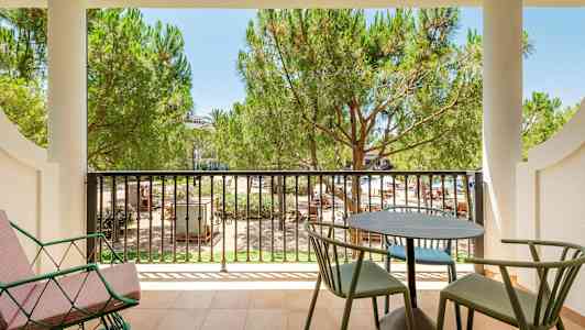 En altan med bord, stole og udsigt til frodige træer. (AI-genereret tekst)