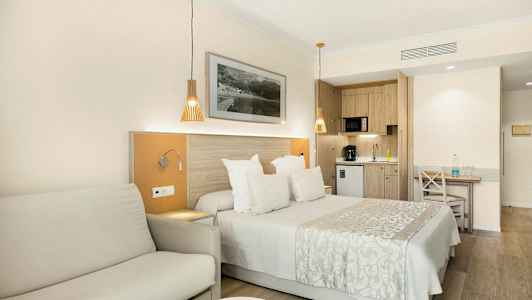 Et hotelværelse med en dobbeltseng, sofa og et køkken i baggrunden. (AI-genereret tekst)