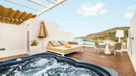 En terrasse med boblebad, liggende møbler og udsigt over havet og landskabet. (AI-genereret tekst)