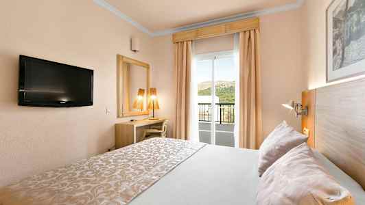 Et hotelværelse med dobbeltseng, TV, skrivebord, spejl og en balkon med udsigt. (AI-genereret tekst)