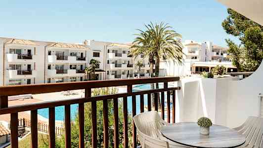 Udsigt fra altan med bord og stole mod hvid bygning og poolområde. (AI-genereret tekst)