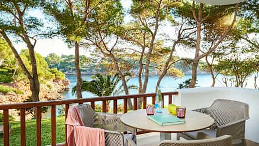 Udendørs veranda med bord og stole, udsigt over træer og hav. (AI-genereret tekst)