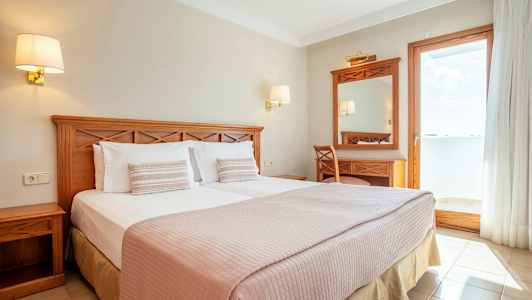 Dobbeltværelse med træmøbler og udsigt til en solrig altan. (AI-genereret tekst)