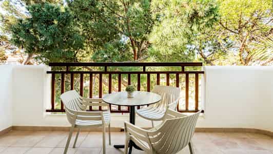 En altan med fire stole og et bord foran et rækværk og grønne træer. (AI-genereret tekst)