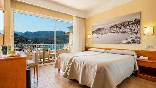 Et hotelværelse med to enkeltsenge, et stort vindue med udsigt til en bjergskråning og en balkon med stole. (AI-genereret tekst)